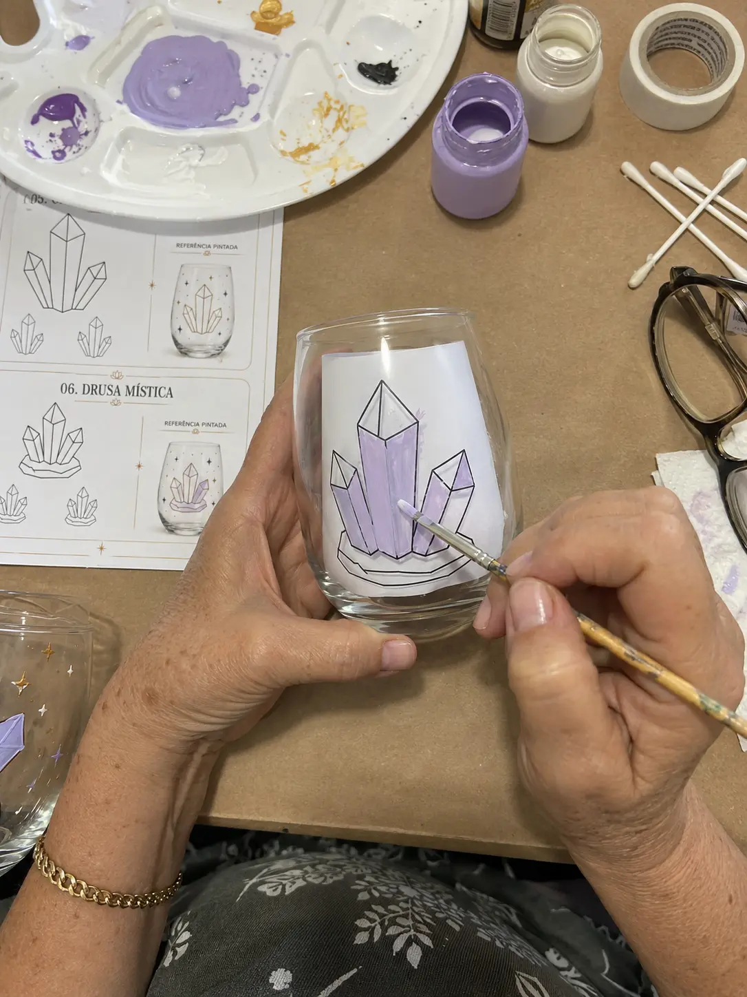 Manos pintando cristales lilas en la copa junto a la lámina del molde
