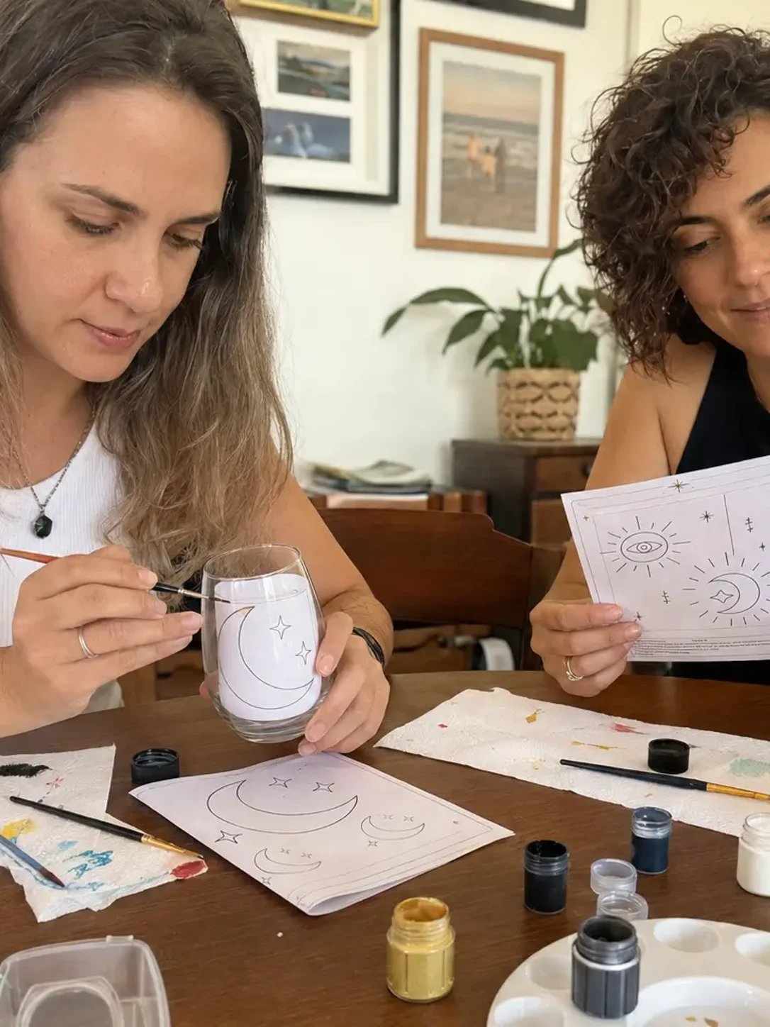 Dos amigas pintando copas con lunas y estrellas usando los moldes